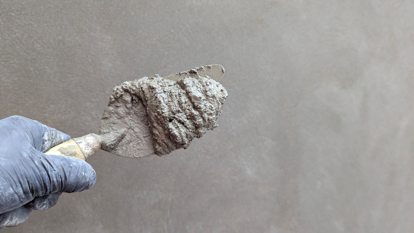 Hands applying joint compound to a wall with a trowel