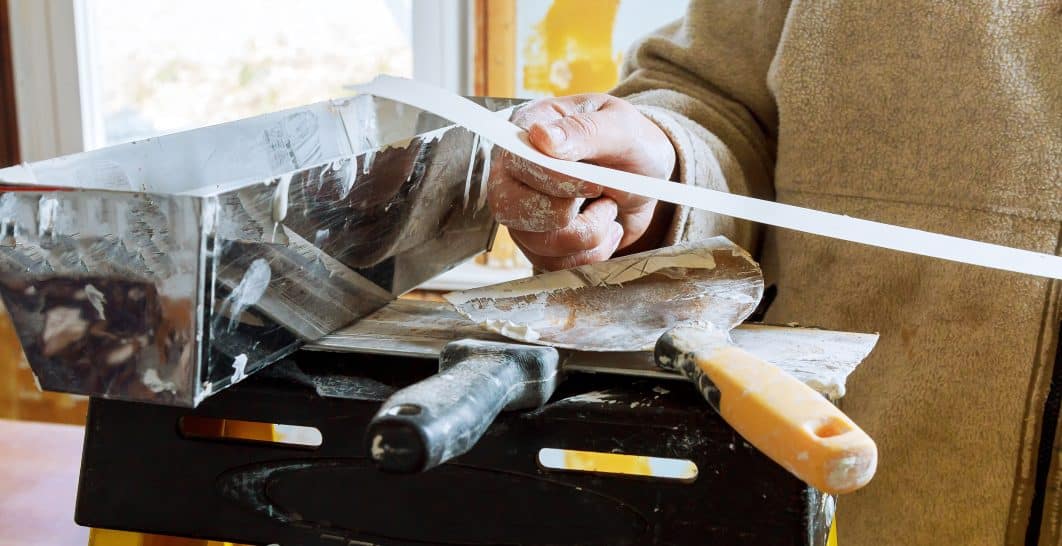 Person using hand plane to smooth wood on workbench near sunny window