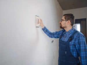 man in a blue attire repairing drywall
