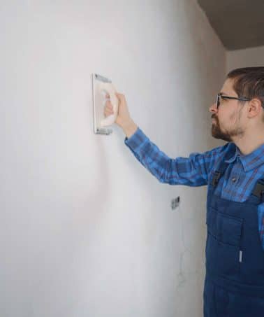 man in a blue attire repairing drywall