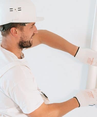 Contractor installing a sheet of drywall on an interior wall in a New Orleans home