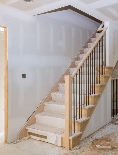 Wooden staircase with metal railings under construction in unfinished white-walled interior space