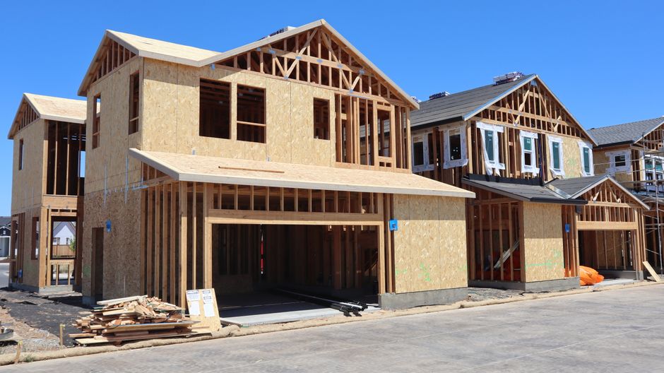 Wide shot of an open, freshly framed new-construction interior with drywall sheets staged against the studs, natural lig
